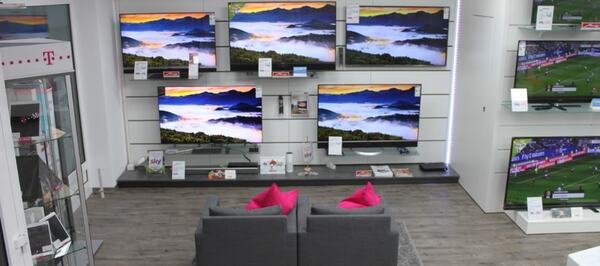 Moderne Fernseher in einem Elektronikfachgeschäft mit gemütlicher Sitzgelegenheit davor.